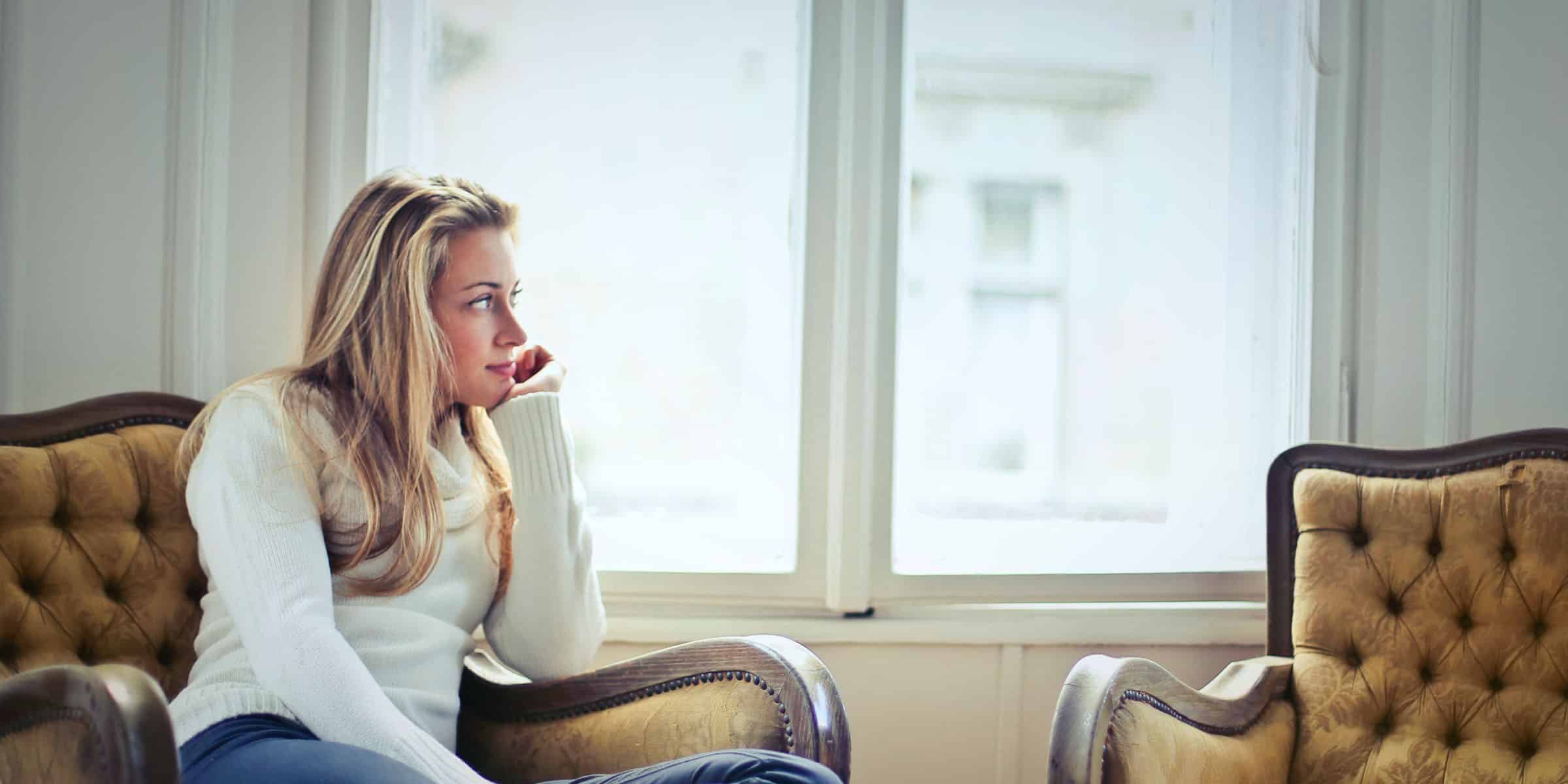 young white woman sitting in wingback chair looking at double windows